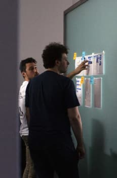 Two people working on a flowchart hanged on a wall through the help of posts it